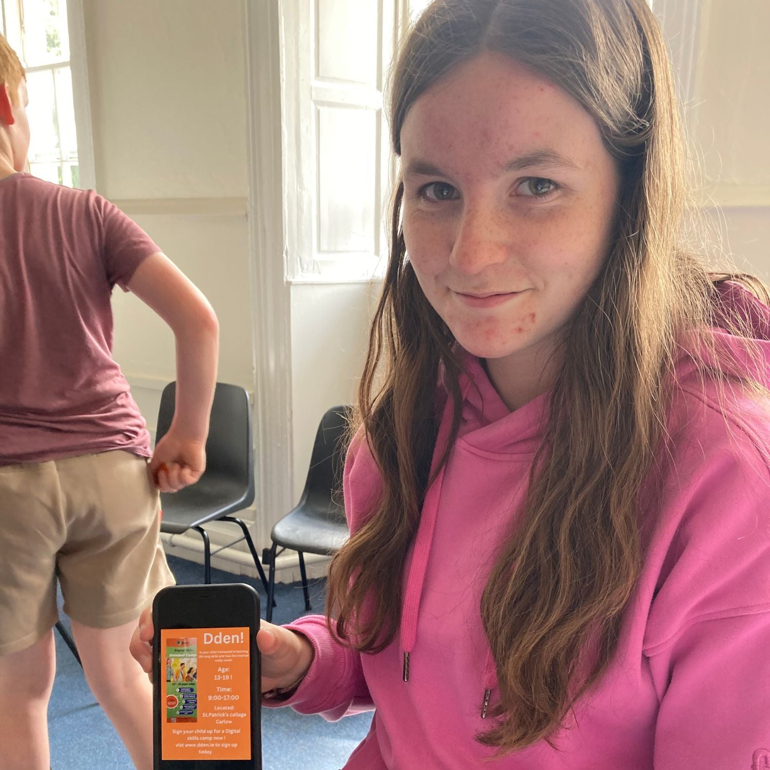 teenage girl holding iphone with a dden summer camps poster she made on canva
