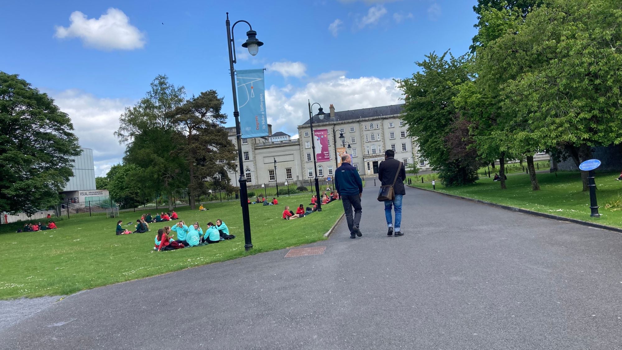 Dr-Immanuel-Darkwa-walking-towards-carlow-college-with-students-sitting-with-friends--on-the-grass